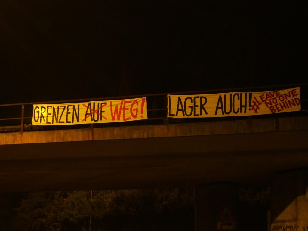 Banner mit Aufschrift: "Grenzen auf (durhgestrichen) weg! Lager auch! # Leave No One Behind